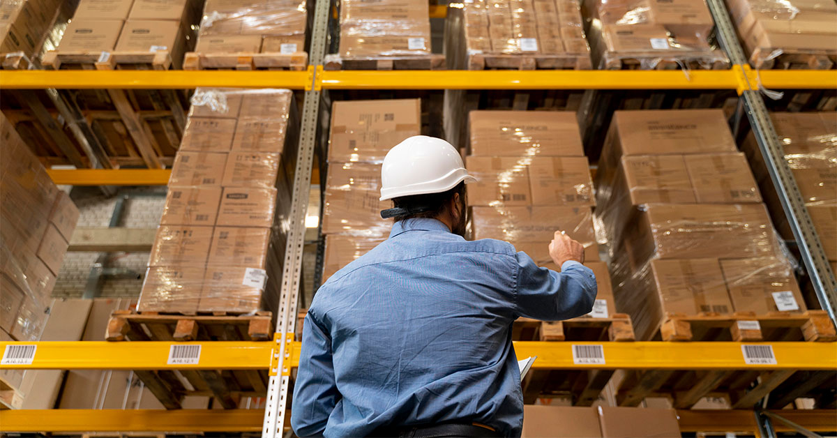 Man in fulfillment centre wearing a blue shirt and a white hard hat